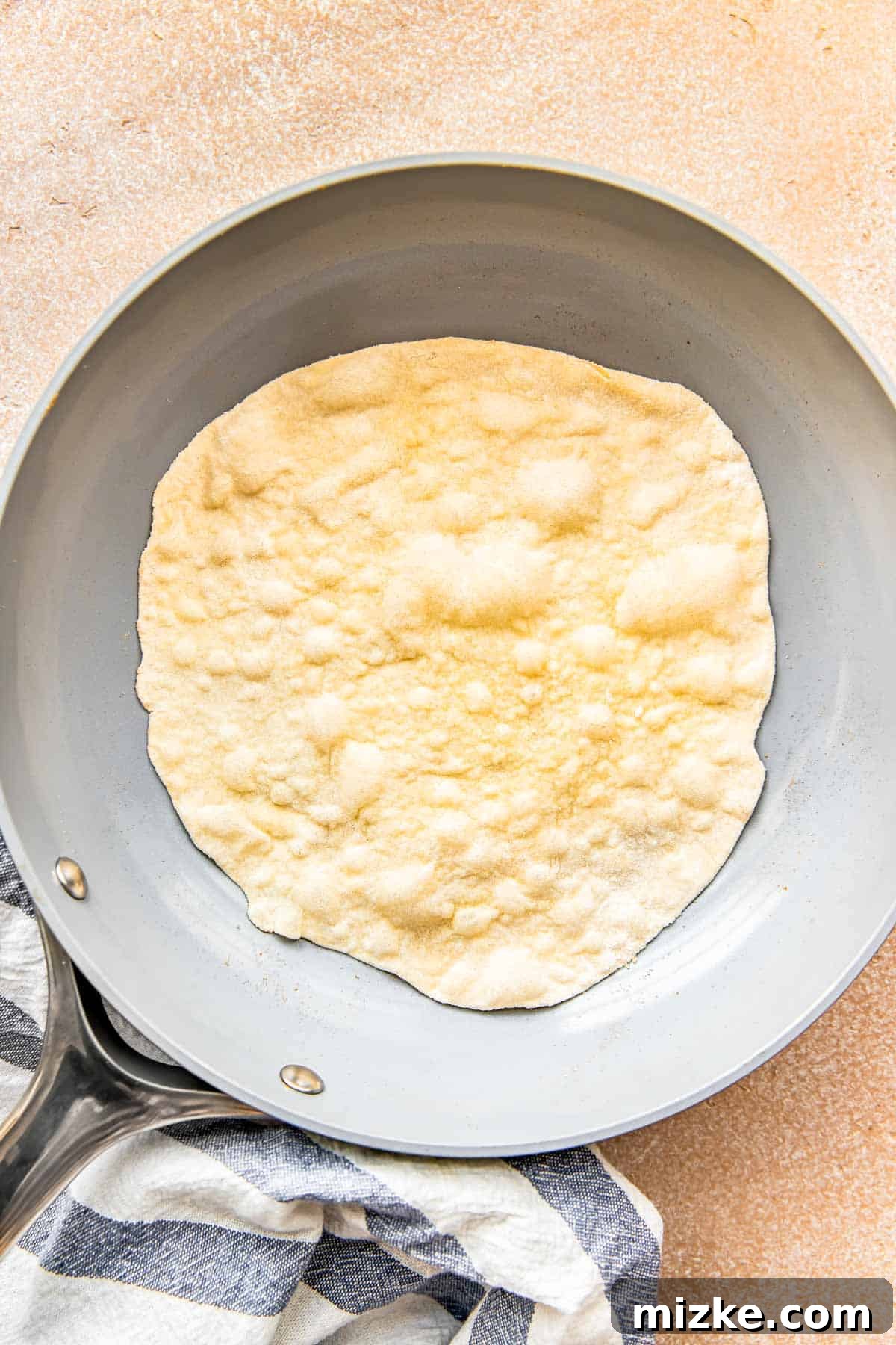 Craft Your Own Perfect Flour Tortillas 7 A homemade flour tortilla sizzling in a nonstick skillet, with numerous bubbles appearing on its surface.