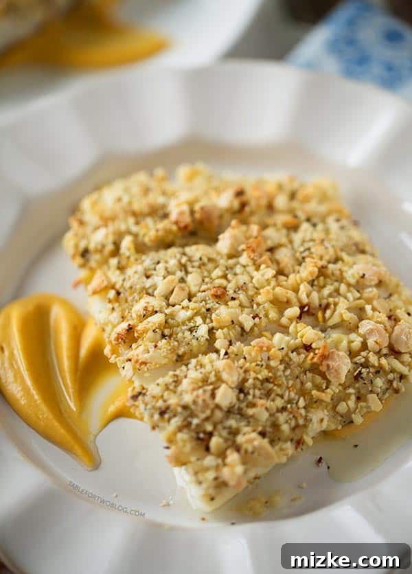 Baked Halibut with Almond Crust and Pumpkin Sweet Potato Puree: An easy, impressive, and delicious fish dinner idea. Three baked almond-crusted halibut fillets on a plate over a bed of sweet potato puree, garnished with fresh herbs.