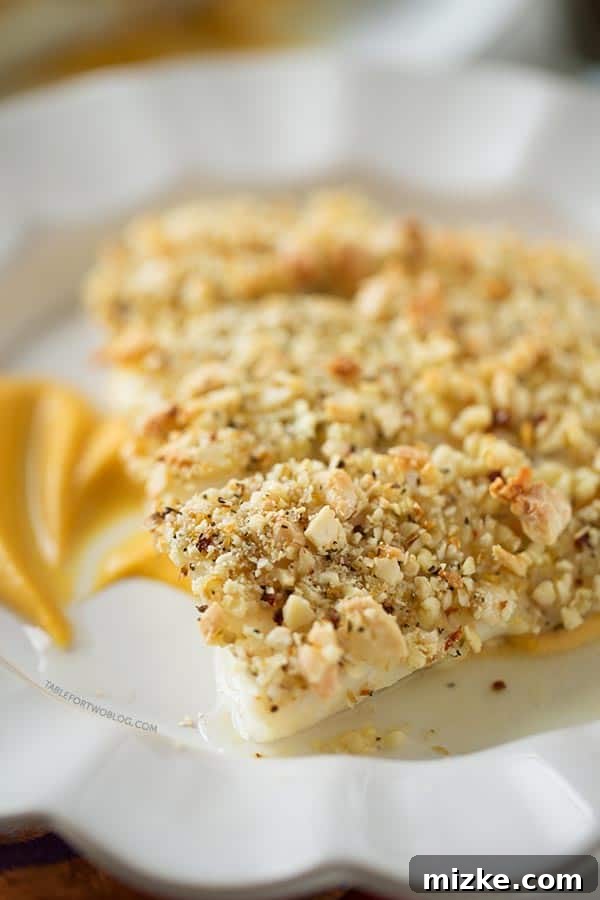 A close-up view of the perfectly golden and crunchy almond crust on baked halibut, resting on a smooth pumpkin sweet potato puree. Close-up of baked almond-crusted halibut fillet showing the crunchy texture, served with a generous scoop of sweet potato puree.