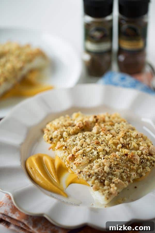 Detail shot of the crisp almond crust on a baked halibut fillet, highlighting its inviting texture. Side view of a single baked almond-crusted halibut fillet showcasing the crust and flakiness, on a bed of puree.