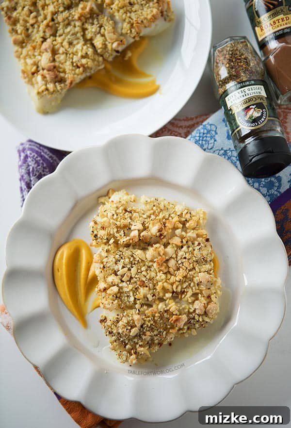 A beautifully plated dish of baked halibut with almond crust and pumpkin sweet potato puree, ready for a delightful meal. Overhead view of two plates with baked almond-crusted halibut fillets served over a generous portion of sweet potato puree, garnished with fresh herbs.