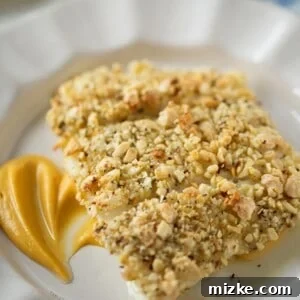 Three baked almond-crusted halibut fillets on a plate over a bed of sweet potato puree.