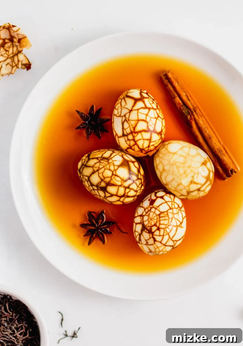 Taiwan's Fragrant Marbled Eggs 4 Overhead shot of marbled Taiwanese tea eggs all peeled on a white plate with braising liquid, star anise, and cinnamon stick.