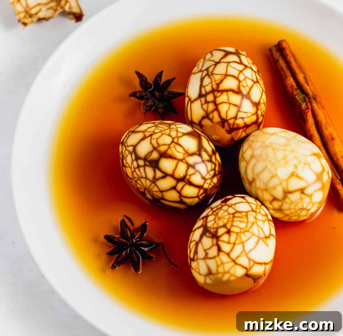 Taiwan's Fragrant Marbled Eggs 5 Up close shot of marbled Taiwanese tea eggs all peeled on a white plate with braising liquid, star anise, and cinnamon stick.