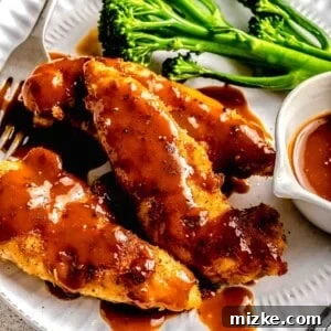 Closeup of bourbon chicken on a plate with broccoli, extra sauce, and a fork.