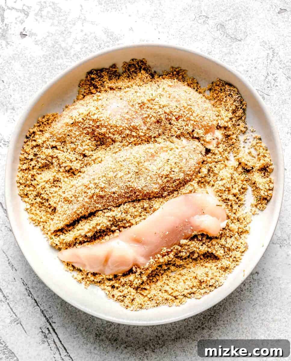 Achieving the perfect crispy coating for bourbon chicken by thoroughly breading each tenderloin. Coating chicken tenderloins with a breadcrumb mixture in a baking dish.