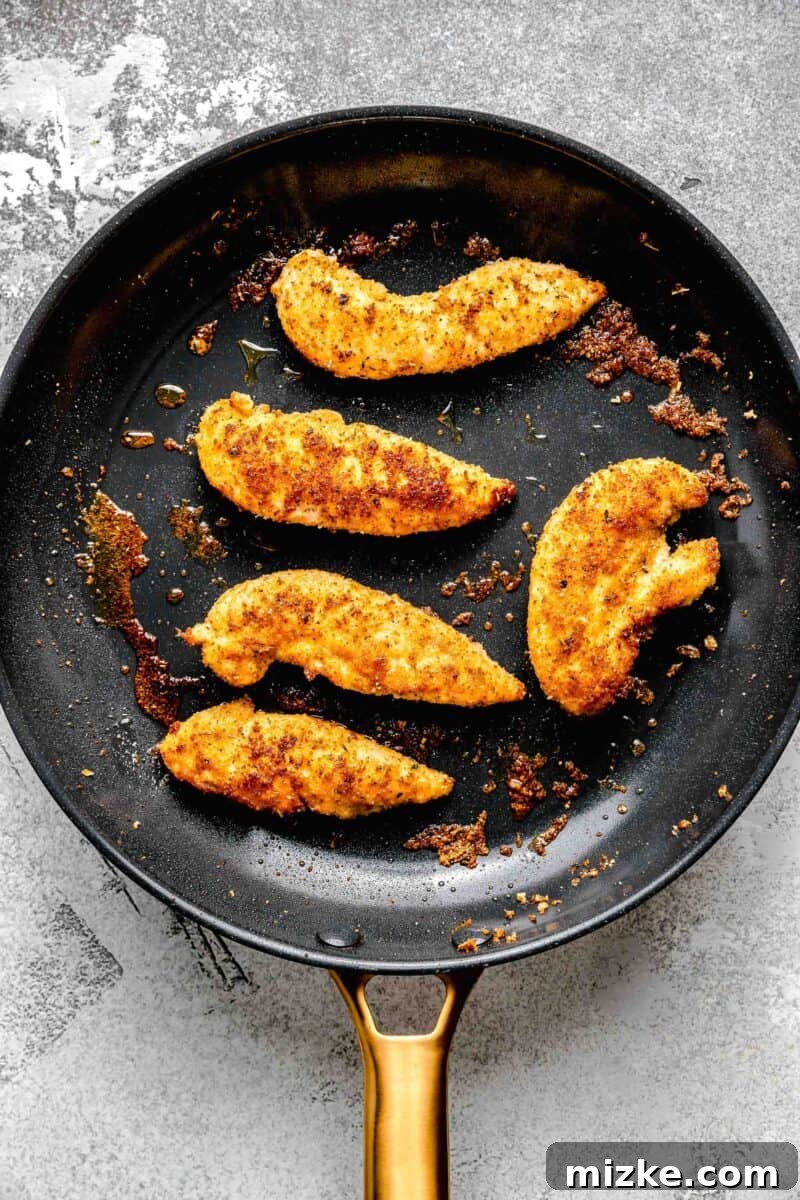 The exquisite transformation of breaded chicken tenderloins as they achieve a perfect pan-fried crisp. Pan-frying golden-brown breaded chicken tenderloins in a skillet.