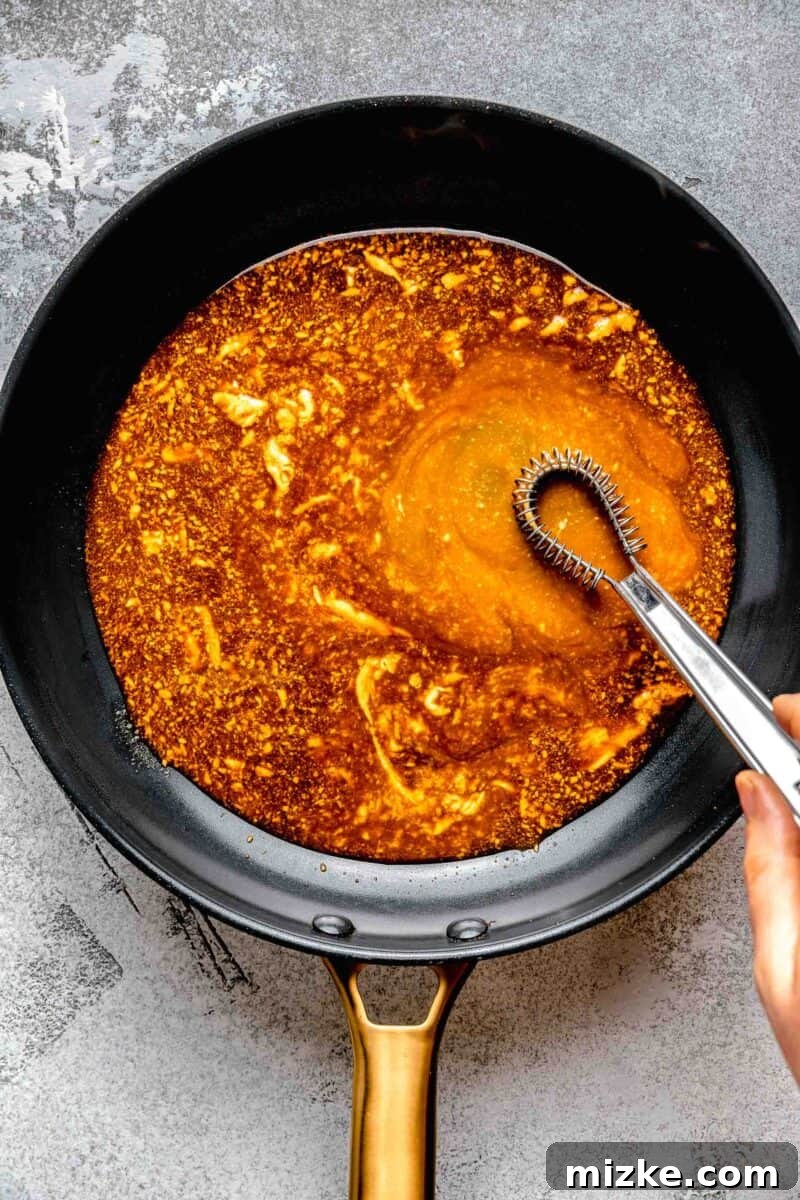 The final touches: whisking butter into the sweet and savory sauce for a perfect bourbon chicken glaze. Expertly whisking chilled butter into the bourbon sauce in a pan to create a smooth, glossy consistency.