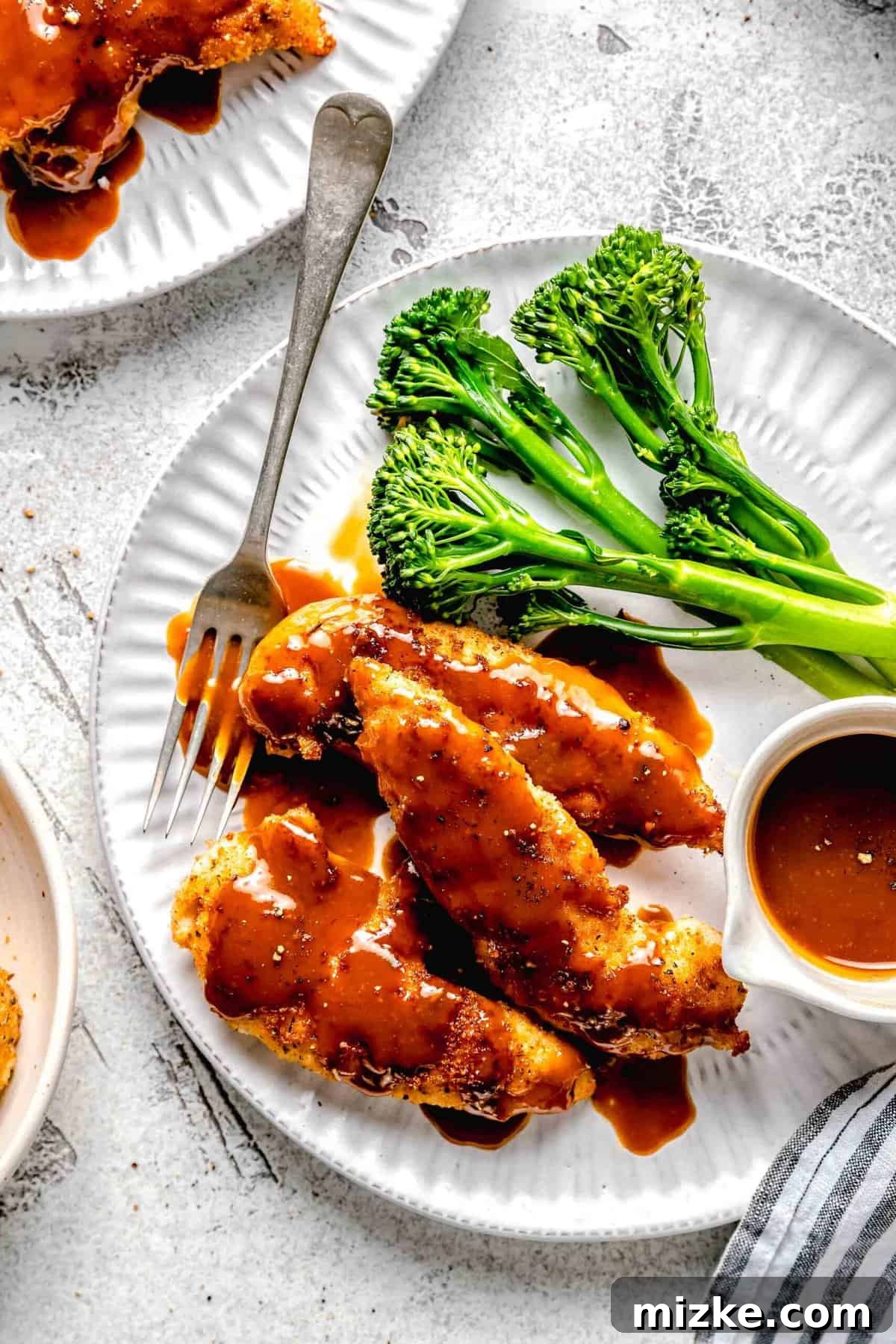 A close-up view of the perfectly glazed bourbon chicken, showcasing its crispy exterior and succulent interior, paired with vibrant greens. Close-up of a serving of bourbon chicken on a plate with steamed broccoli, a pool of extra sauce, and a fork, emphasizing its delicious texture.