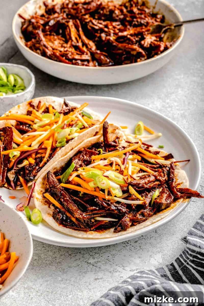 Slow Cooked Korean BBQ Pork Tacos 4 Two beautifully plated Korean pork tacos, generously topped with crisp, fresh slaw and a sprinkle of green onions.