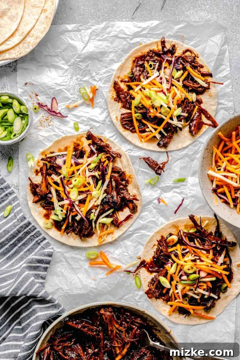 Slow Cooked Korean BBQ Pork Tacos 5 A close-up of several Korean pork tacos, generously loaded with succulent shredded pork and refreshing tangy slaw.