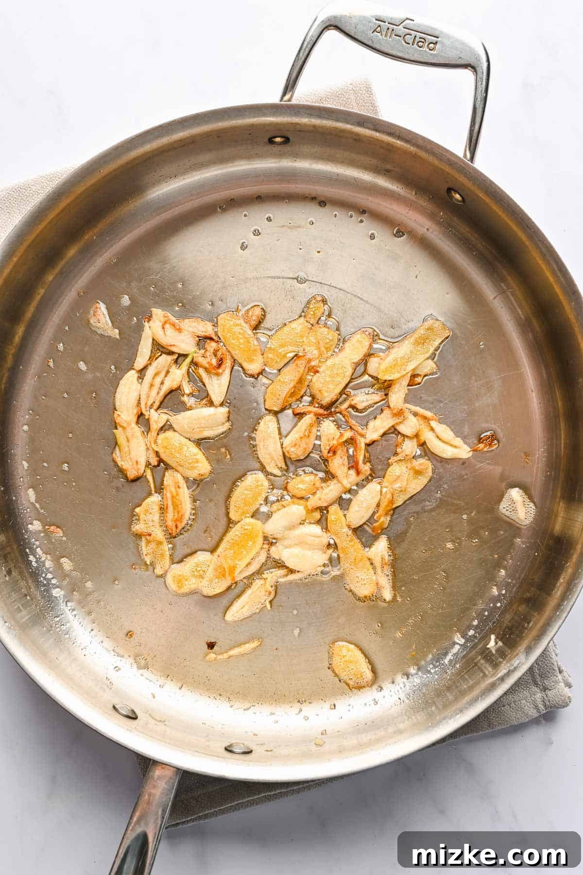 This authentic Taiwanese recipe for three cup chicken (三杯雞) is easy enough to make at home, so you won't have to get it from a restaurant! Overhead view of smashed garlic cloves sauteing in a metal skillet.