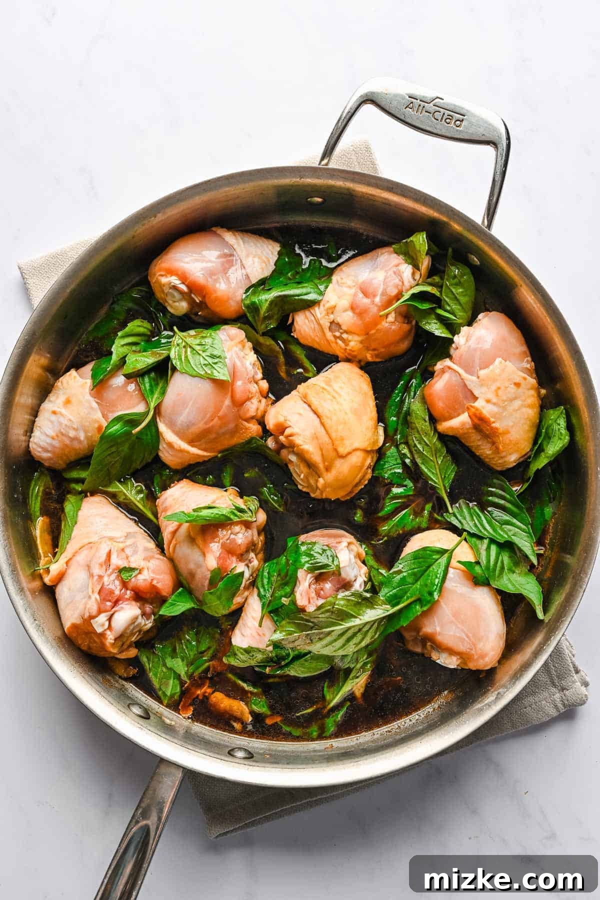 This authentic Taiwanese recipe for three cup chicken (三杯雞) is easy enough to make at home, so you won't have to get it from a restaurant! Chicken drumstick halves and fresh basil leaves added to a large skillet with garlic.