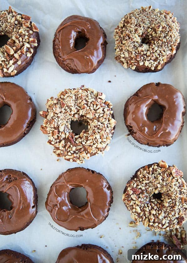 Decadent Double Chocolate Donuts Close-up of freshly made chocolate chocolate donuts with ganache glaze, some topped with pecans, on a white plate