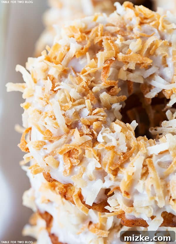 Freshly fried Triple Coconut Donut being dipped into a sweet coconut glaze