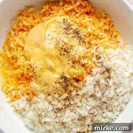 Irresistible Cheesy Hashbrown Bake 5 A large bowl contains melted butter, salt, pepper, diced onions, cream of chicken soup, and freshly grated cheese, ready to be mixed.