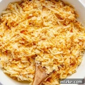 Irresistible Cheesy Hashbrown Bake 6 Thawed shredded hashbrown potatoes being gently mixed into the creamy cheese and cream of chicken soup mixture in a large bowl.