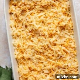 Irresistible Cheesy Hashbrown Bake 7 The unbaked cheesy hashbrown casserole mixture spread evenly in a white casserole dish, ready for the oven.