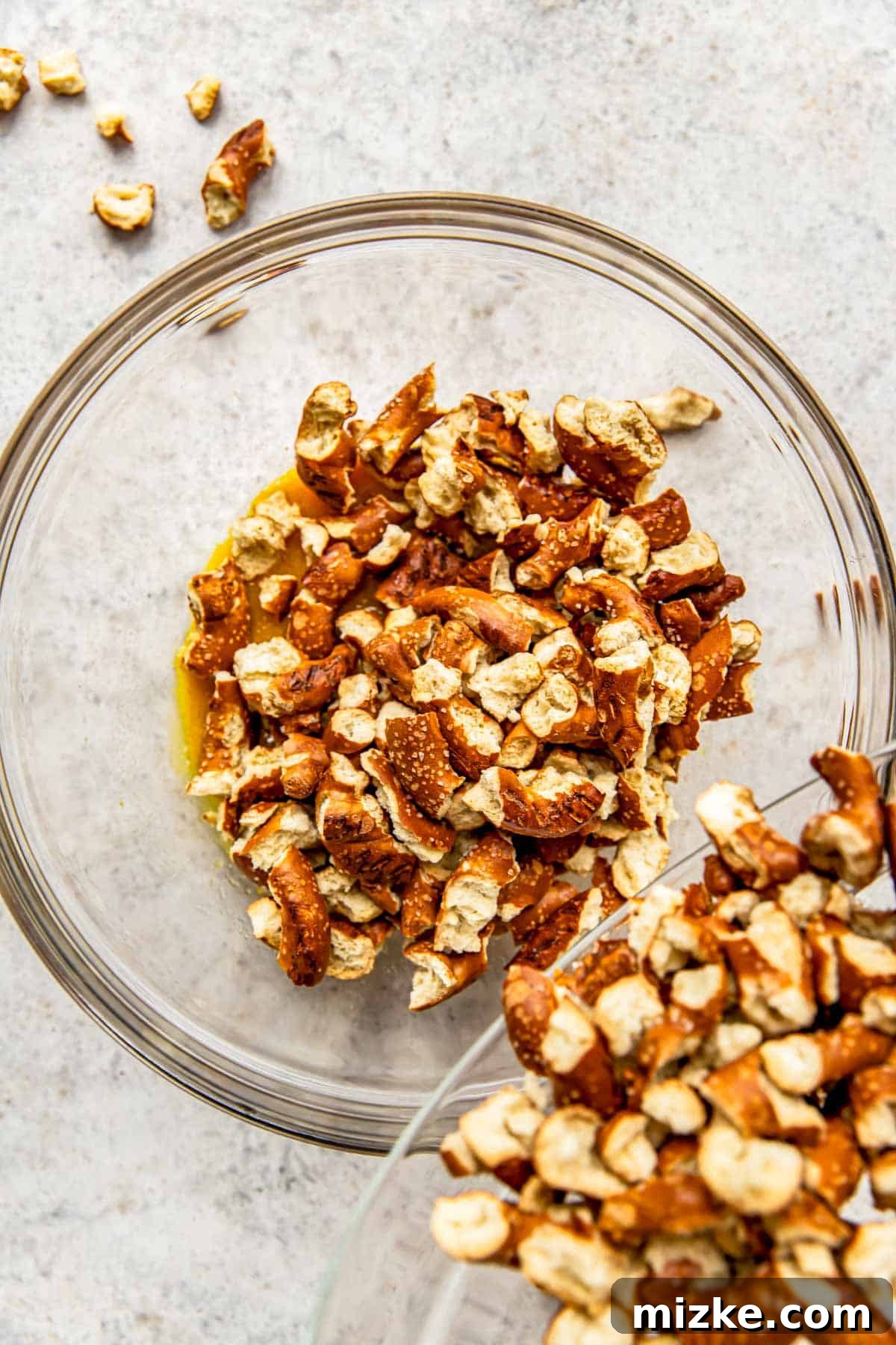 Tangy Gold Pretzel Crunch 6 Bite-sized pretzel pieces are carefully added to a glass bowl, ready to be coated in the flavorful honey mustard sauce.
