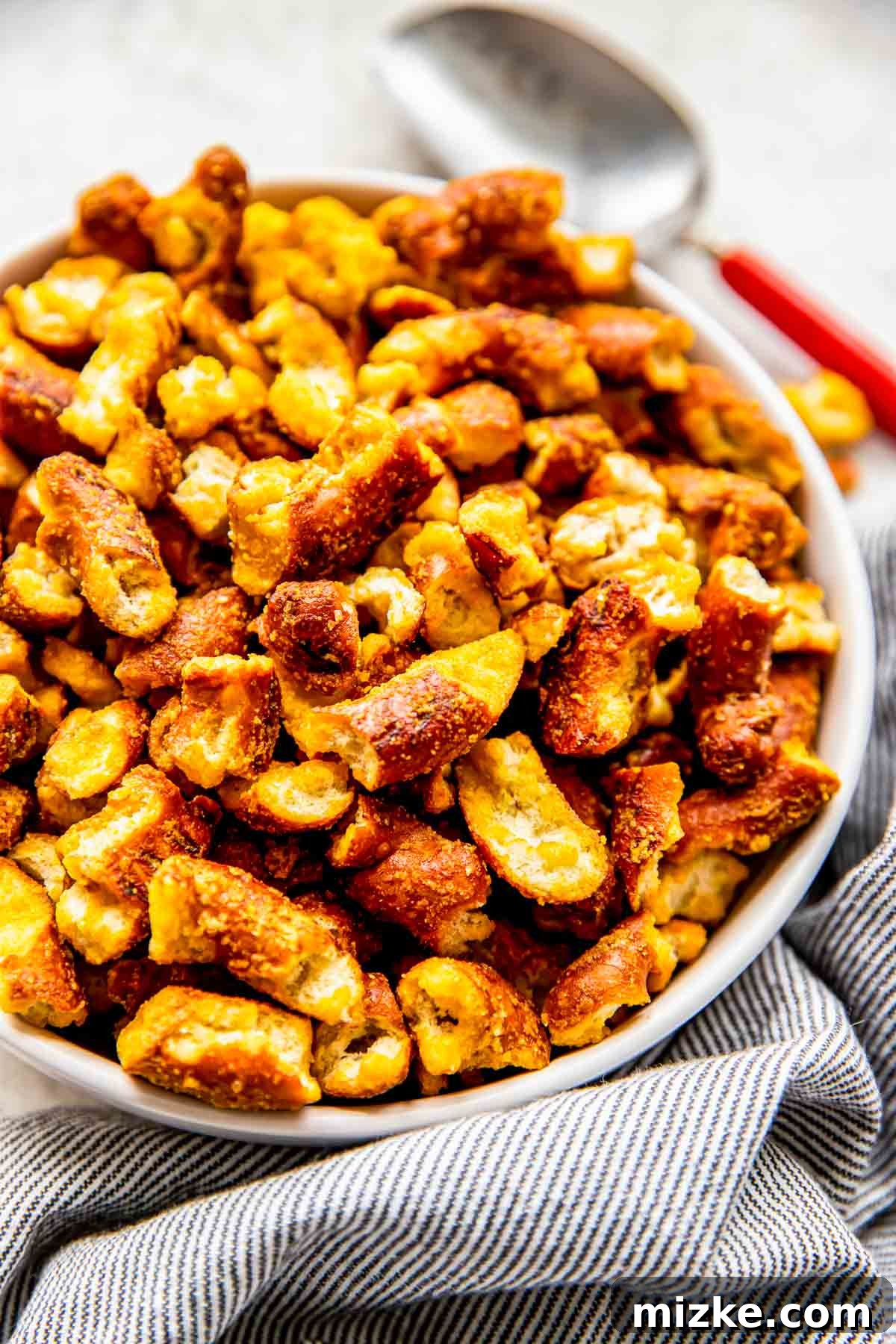 Tangy Gold Pretzel Crunch 9 A serving scoop rests beside a full bowl of crispy, golden honey mustard pretzels, ready to be enjoyed.