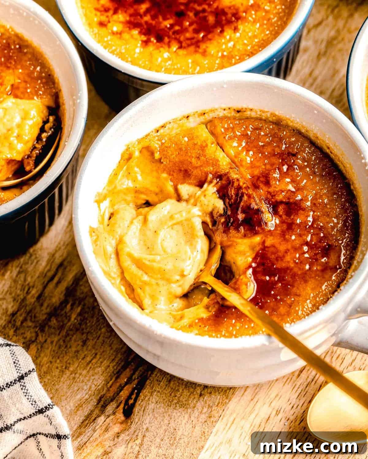 Creamy, restaurant-quality pumpkin creme brulee is infused with just the right amount of pumpkin & has the perfect caramelized sugar topping. A spoon breaking through the caramelized sugar topping of a pumpkin creme brulee, revealing the creamy custard beneath.
