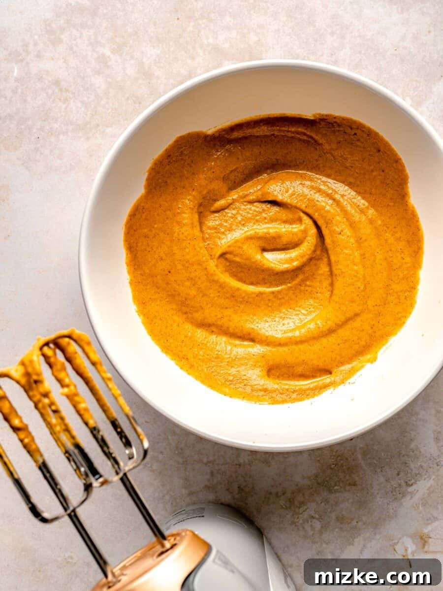 Creamy, restaurant-quality pumpkin creme brulee is infused with just the right amount of pumpkin & has the perfect caramelized sugar topping. Close-up shot of egg yolks, pumpkin puree, pumpkin pie spice, and brown sugar being whisked together in a bowl for pumpkin creme brulee.