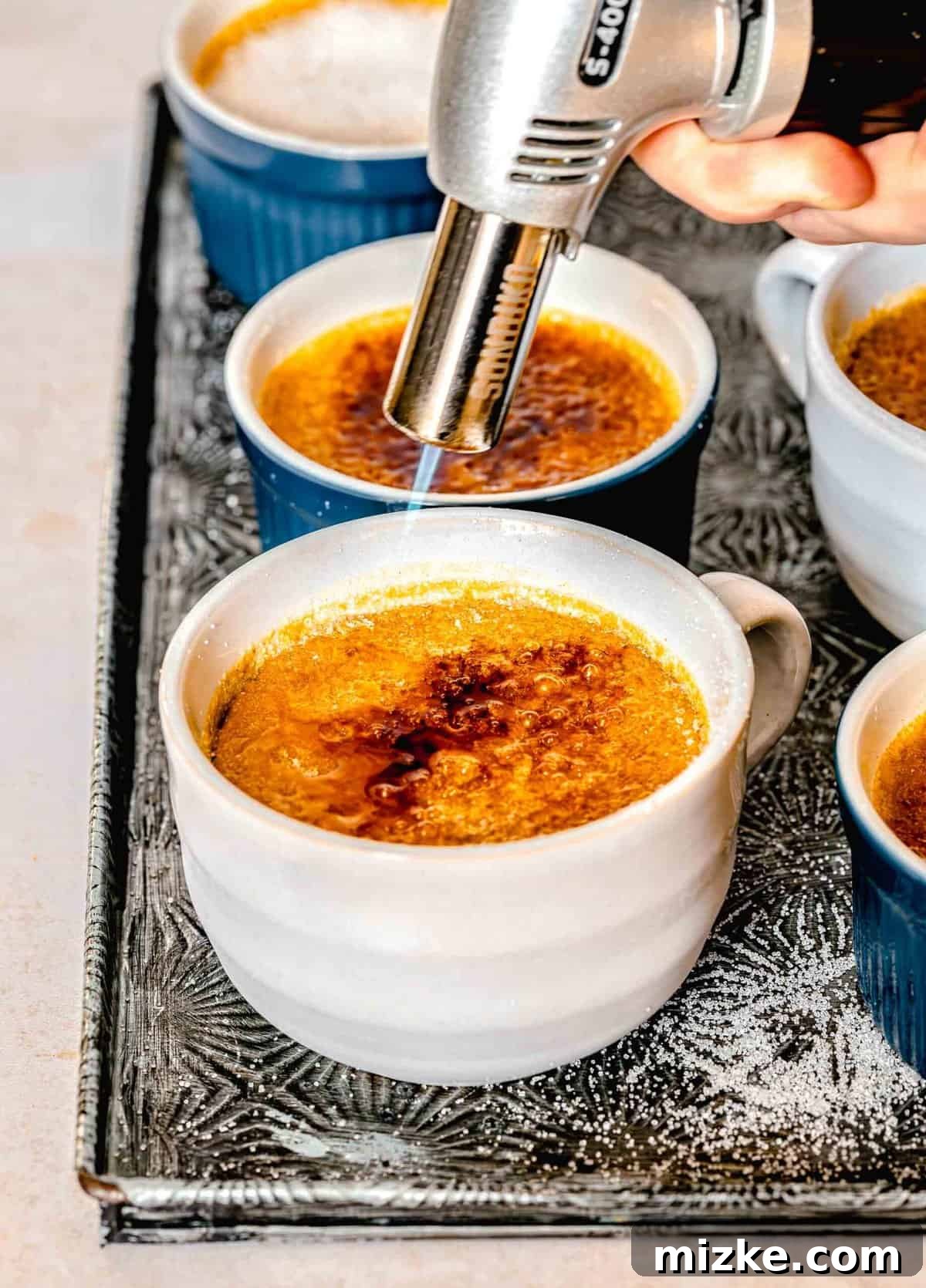 Creamy, restaurant-quality pumpkin creme brulee is infused with just the right amount of pumpkin & has the perfect caramelized sugar topping. A kitchen torch caramelizing the granulated sugar topping on a pumpkin creme brulee in a ramekin.