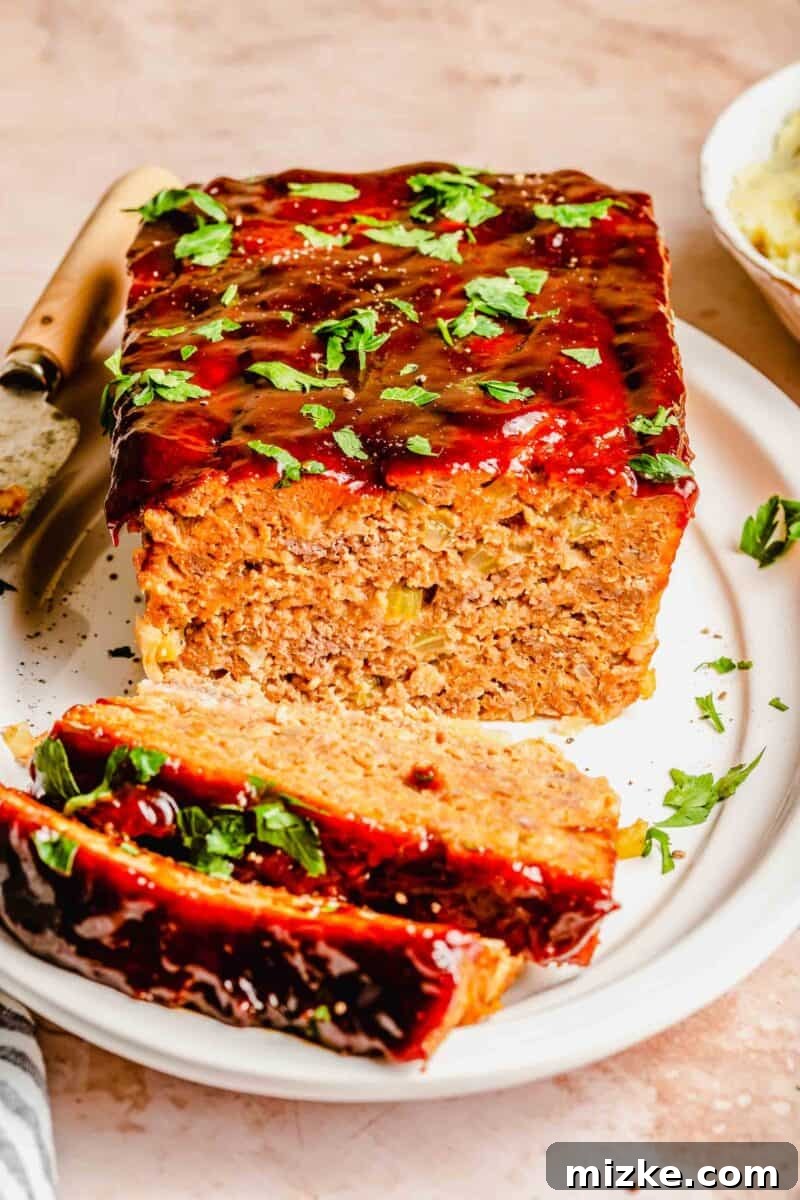 This perfectly baked classic meatloaf is ideal for weeknights. Enjoy its comforting, delicious, and moist texture with a sweet and tangy sauce. A large slice of classic meatloaf resting on a wooden cutting board with a serving knife beside it, showcasing its moist interior and savory glaze.