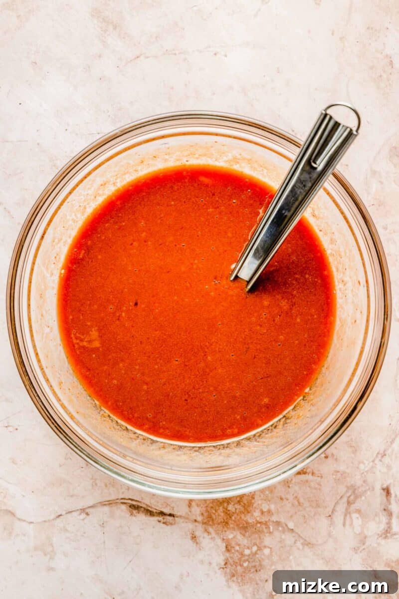 The perfectly mixed wet ingredients for classic meatloaf: eggs, milk, Worcestershire sauce, and a portion of the sweet and tangy glaze. The savory liquid sauce mixture in a bowl, stirred with a spoon, ready to be added to the meatloaf.