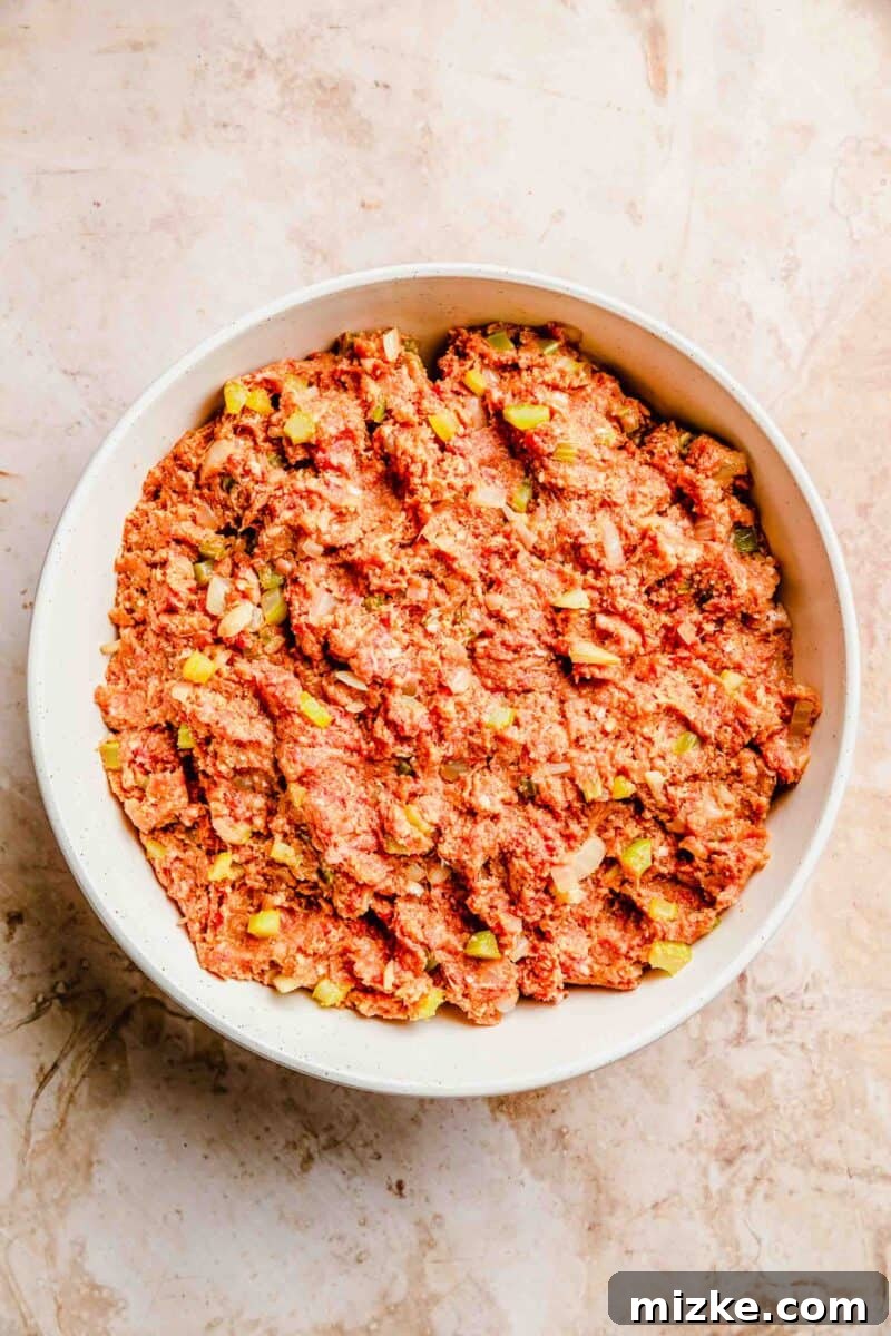The classic meatloaf mixture, pre-assembly, showcasing ground beef, breadcrumbs, sautéed veggies, and wet binders blended together. A large bowl containing the raw meatloaf mixture, including ground beef, breadcrumbs, and sautéed vegetables, ready for assembly.