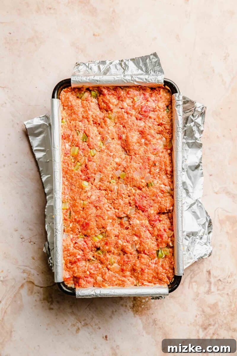 Meatloaf assembled in a loaf pan, perfectly shaped and ready for the final glazing before baking into a delicious weeknight meal. The classic meatloaf mixture firmly pressed into a foil-lined loaf pan, ready for glazing and baking.