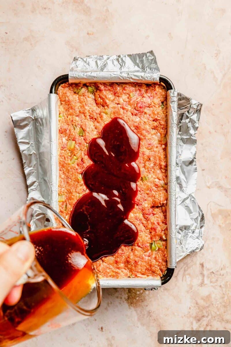 Glaze the classic meatloaf liberally before baking to ensure a delicious, caramelized, and flavorful crust. The remaining sweet and tangy glaze being generously poured over the raw meatloaf in the loaf pan, prior to baking.