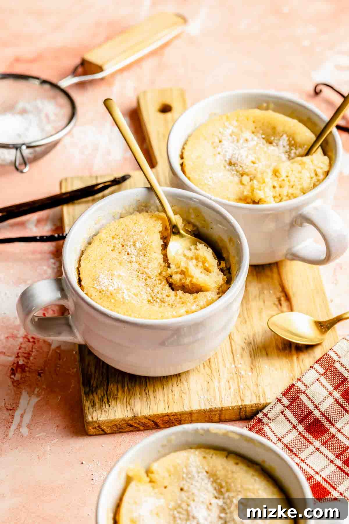 Pure Vanilla Mug Cake 3 Three vanilla mug cakes with golden spoons digging out the cake to display cake texture, showing the moist and fluffy interior.