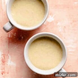 Mug cake batter divided evenly amongst two white mugs, showing the liquid batter before cooking.