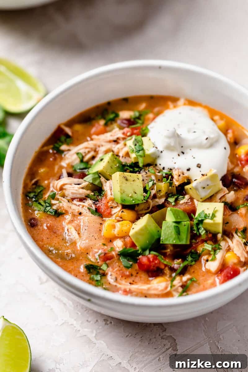 Close-up shot of the rich, red slow cooker chicken enchilada soup simmering, showing tender chunks of chicken, black beans, and sweet corn.
