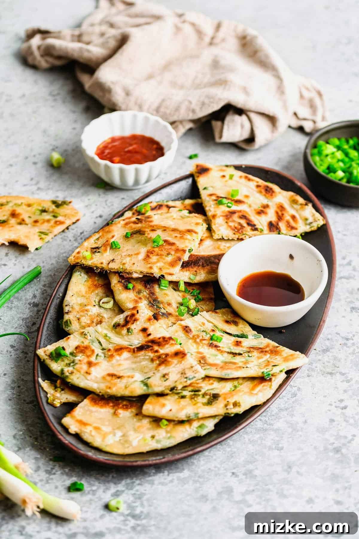 Serve these crispy and chewy scallion pancakes with your favorite dipping sauce for an authentic and satisfying Asian appetizer. Perfectly cut triangles of scallion pancakes arranged on a serving plate, with a small cup of savory dipping sauce beside them.