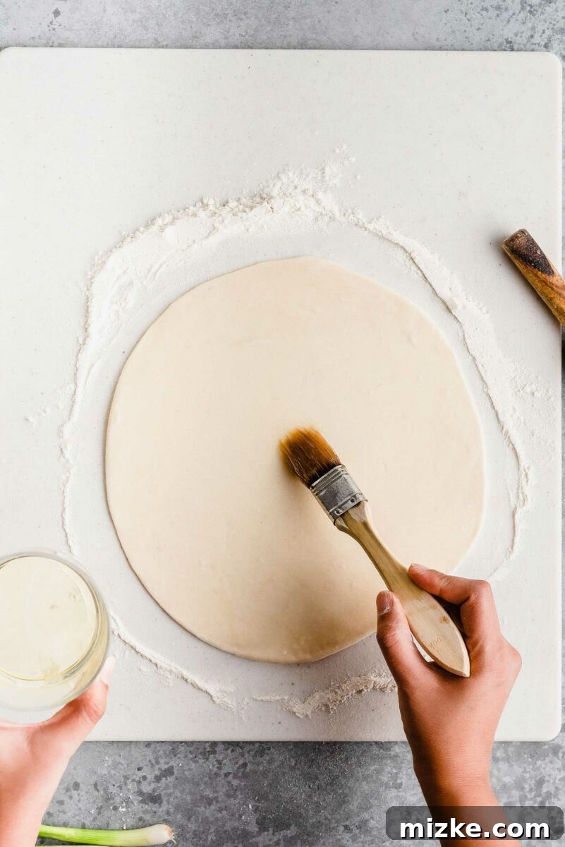 Brushing the dough with oil is a key step to achieve those coveted flaky layers in homemade scallion pancakes. A pastry brush applies a thin, even layer of vegetable oil to the surface of rolled-out scallion pancake dough, preparing it for layering.