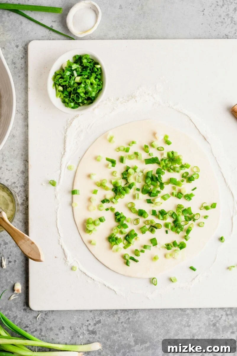 A liberal sprinkling of fresh scallions and salt ensures every bite of your homemade pancake bursts with savory flavor. An overhead view of rolled-out scallion pancake dough generously covered with freshly sliced green onions and a sprinkle of salt.