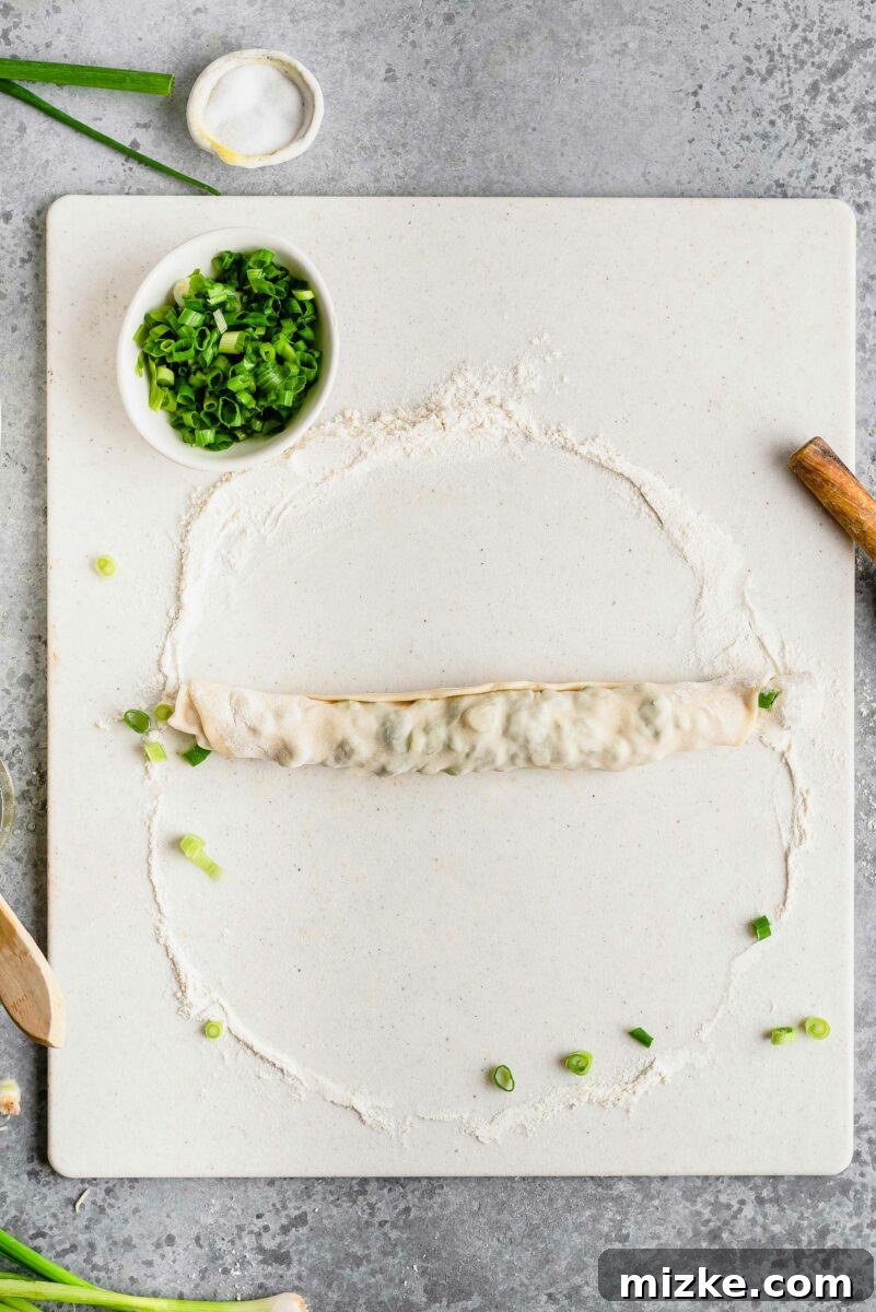 The first step in creating layers: rolling the seasoned dough into a neat log, preparing it for its iconic spiral shape. Overhead view of scallion pancake dough rolled into a log after being oiled and seasoned, ready for coiling.