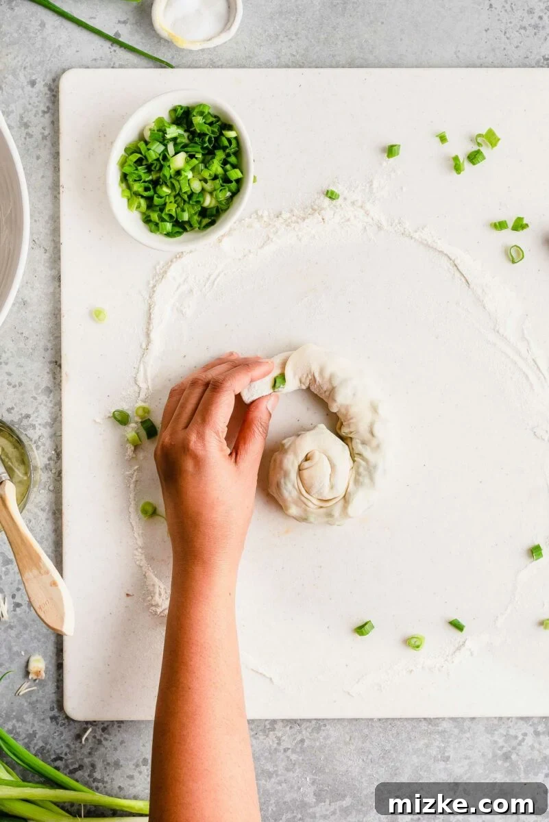 Coiling the dough is essential for developing the flaky, multi-layered texture that defines perfect scallion pancakes. Overhead view demonstrating how scallion pancake dough is twisted and coiled into a spiral, resembling a snail shell, for flaky layers.