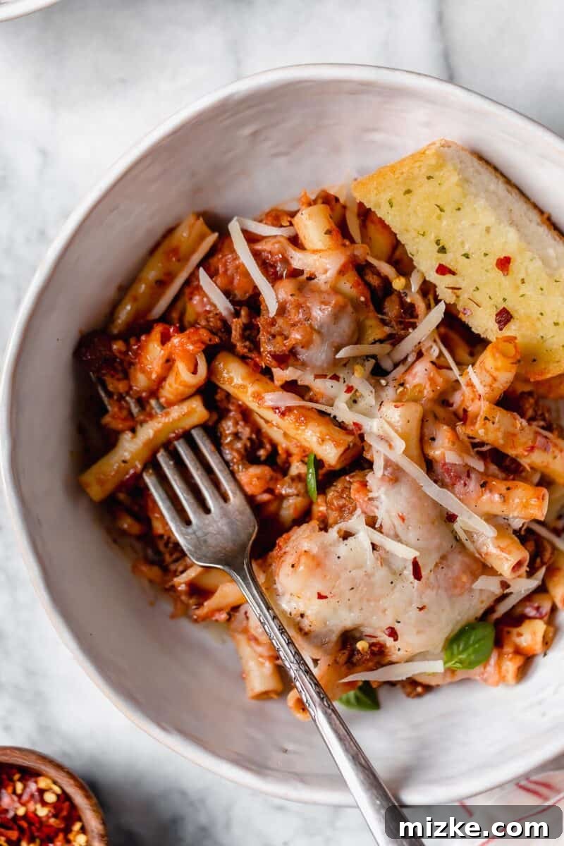 Ultimate Baked Ziti 4 Baked Ziti baking in a white casserole dish, with cheese bubbling and sauce simmering