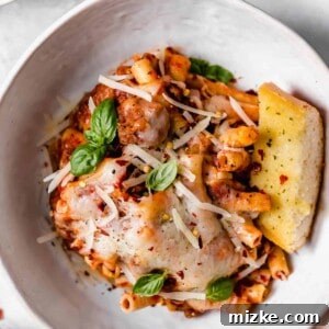 Individual serving of Baked Ziti with golden cheese, garnished with fresh basil, on a white plate