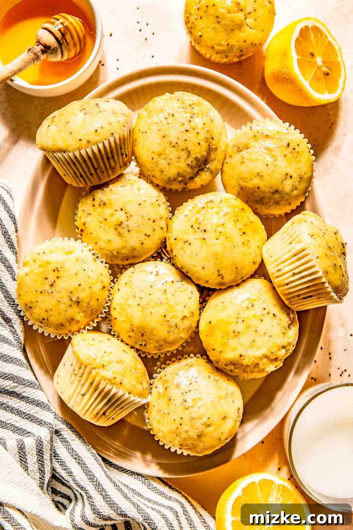 Zesty Lemon Chia Muffins 2 A plate of golden-brown lemon chia seed muffins, garnished with lemon slices and surrounded by a glass of milk and a honey dipper, evoking fresh springtime mornings.