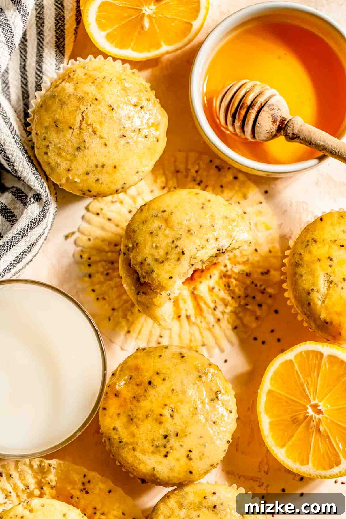 Zesty Lemon Chia Muffins 4 Close-up of freshly baked lemon chia seed muffins in a muffin tin, brushed with honey. Beside them are a glass of milk and sliced lemons, highlighting their fresh appeal.