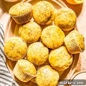 A plate of lemon chia seed muffins is surrounded by a halved lemon, a small dish of honey with a honey dipper, and a glass of milk, inviting you to bake.