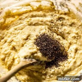 Mixing chia seeds into a bowl of muffin batter with a wooden spoon, showing the seeds being gently incorporated.