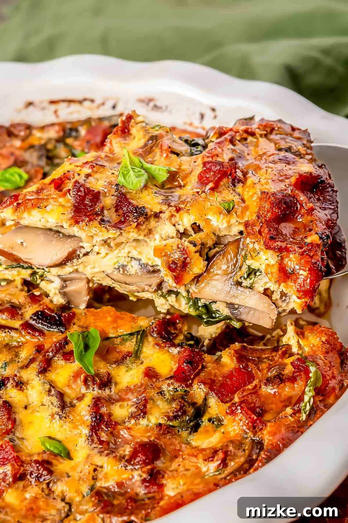 Savory Crustless Bacon, Spinach, and Mushroom Bake 3 a metal serving spoon scoops out a slice of bacon mushroom and spinach quiche