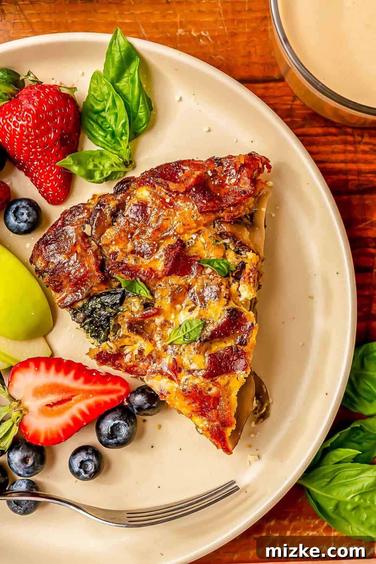 Savory Crustless Bacon, Spinach, and Mushroom Bake 4 a slice of bacon mushroom spinach quiche on a beige plate next to fresh strawberries, blueberries, and apples.