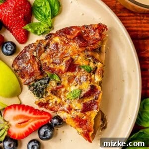 a slice of bacon mushroom spinach quiche on a beige plate next to fresh strawberries, blueberries, and apples.