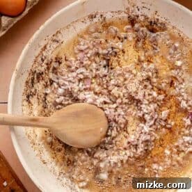 shallots being cooked in bacon grease in a white skillet with a wooden spoon